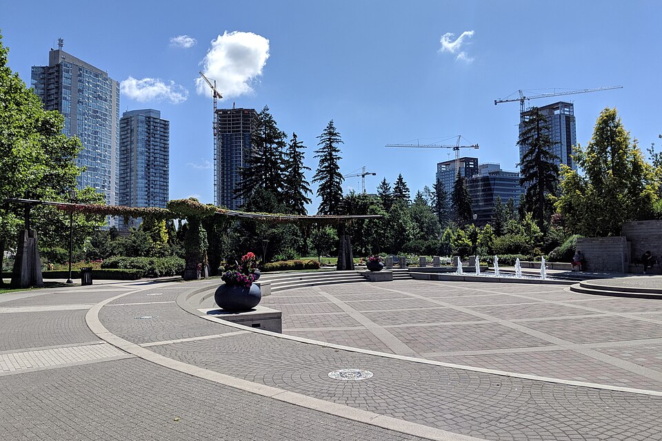 Holland Park plaza, trees and Surrey towers under blue sky.