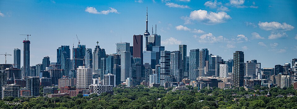 Toronto skyline with shoreline greenery and blue sky.